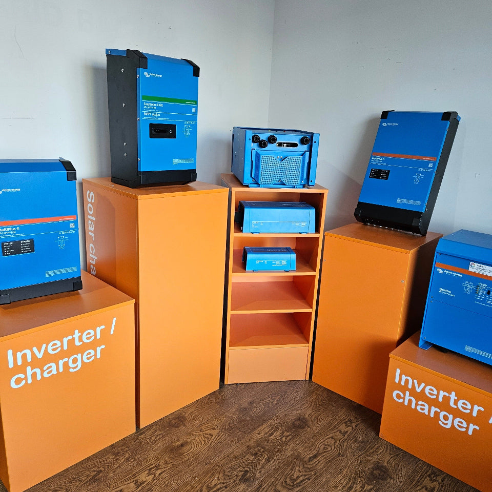 Several blue solar inverters and chargers displayed on orange pedestal boxes in a room corner with wood flooring and white walls.